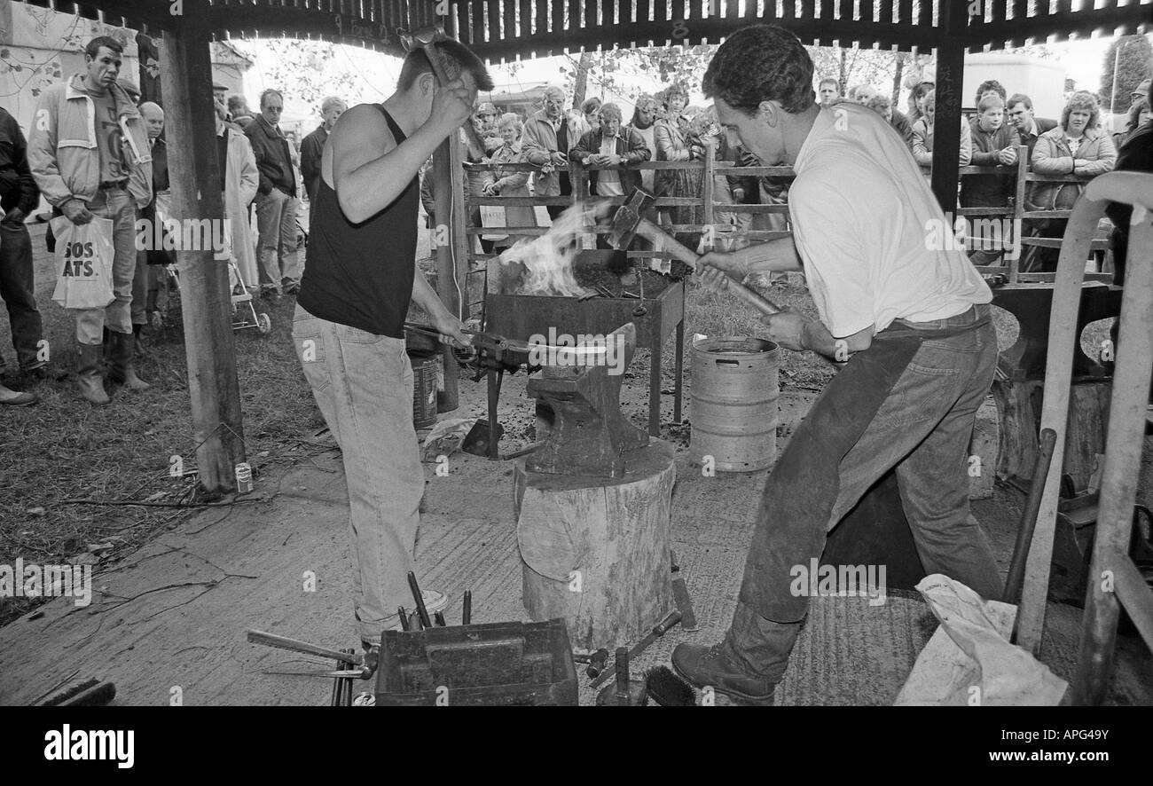 Two young blacksmiths giving demonstation of hammering hot iron bar