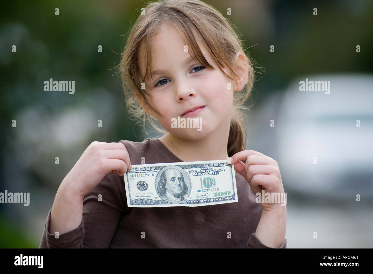 Five year old girl in brown shirt holding hundred dollar bill Stock Photo
