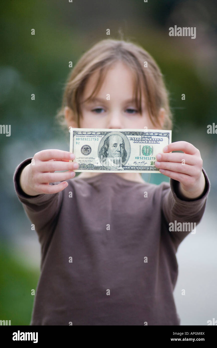 Five year old girl in brown shirt holding $100 bill Stock Photo