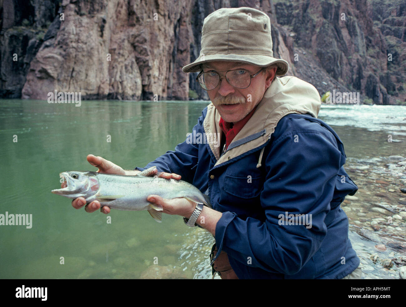 A backpacking fly fisherman holds a large rainbow trout he caught near Phantom Ranch in the Colorado River Stock Photo