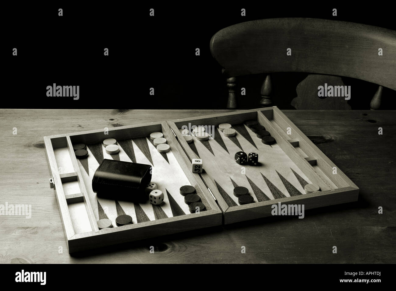 Backgammon set laid out ready for a game on a wooden table with a wooden chair in the background Stock Photo