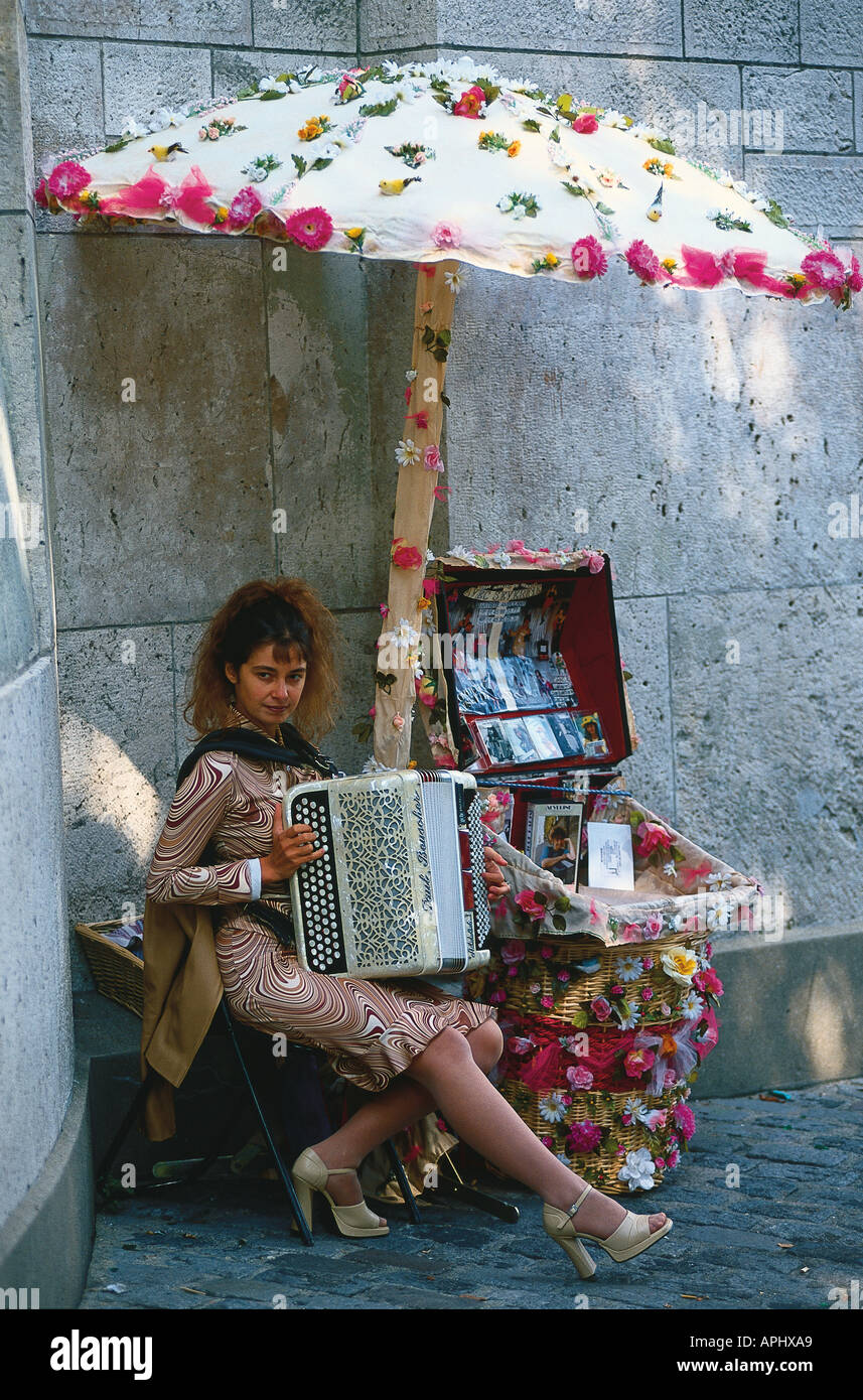 A woman busking in Montmartre playing an accordion under a flower covered umbrella Paris France Stock Photo