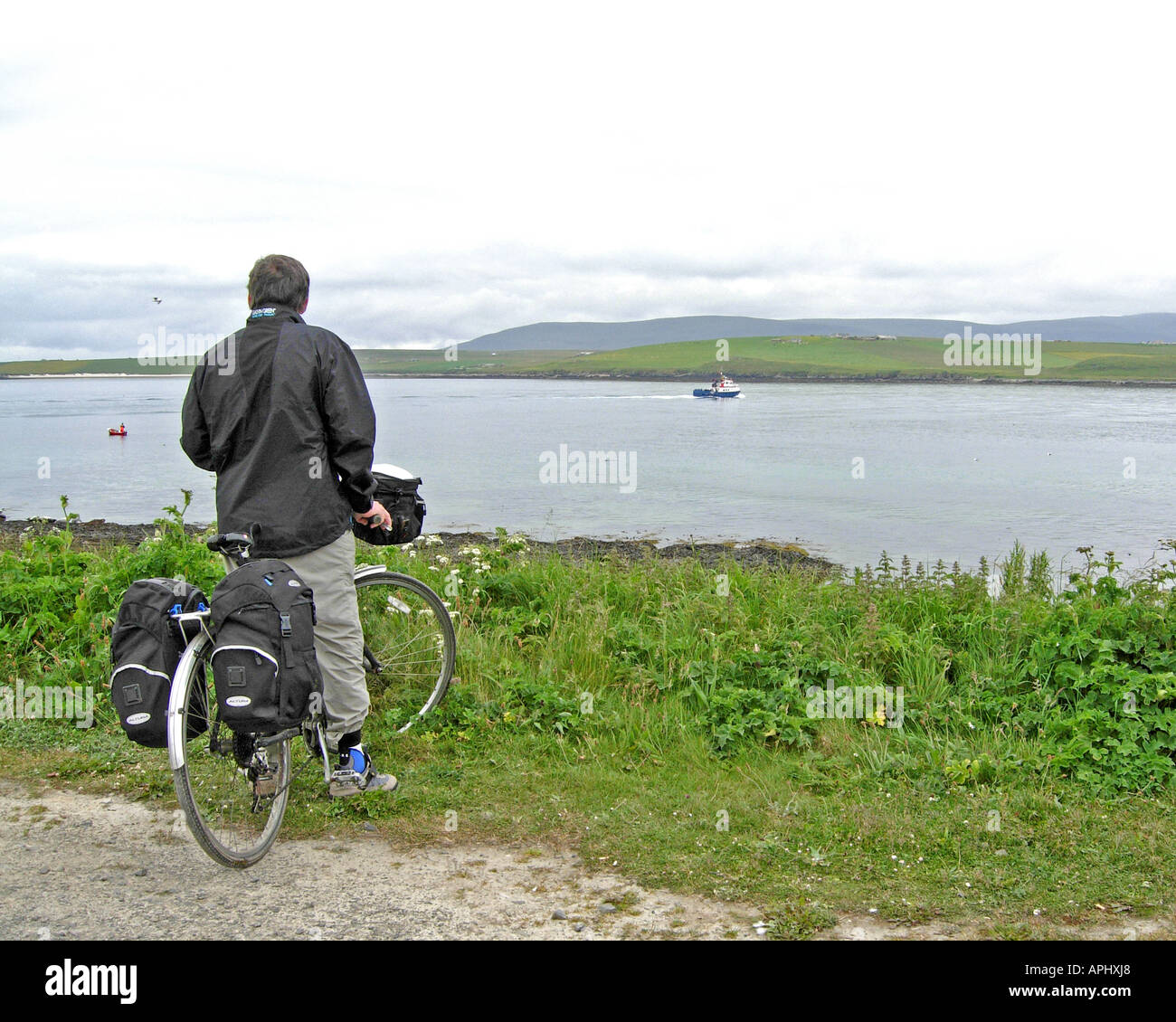 Cyclist watches the Orkney Ferries MV Graemsay sailing out of Stromness passed the island of Graemsay to Hoy via HOY SOUND ORKNE Stock Photo