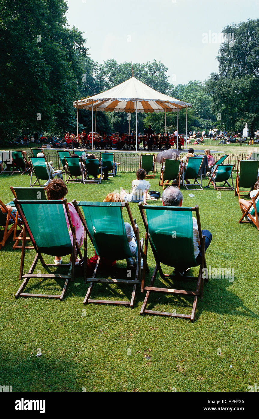 People sat in deckchairs facing the bandstand enjoying the sunshine in Regents Park London England Stock Photo