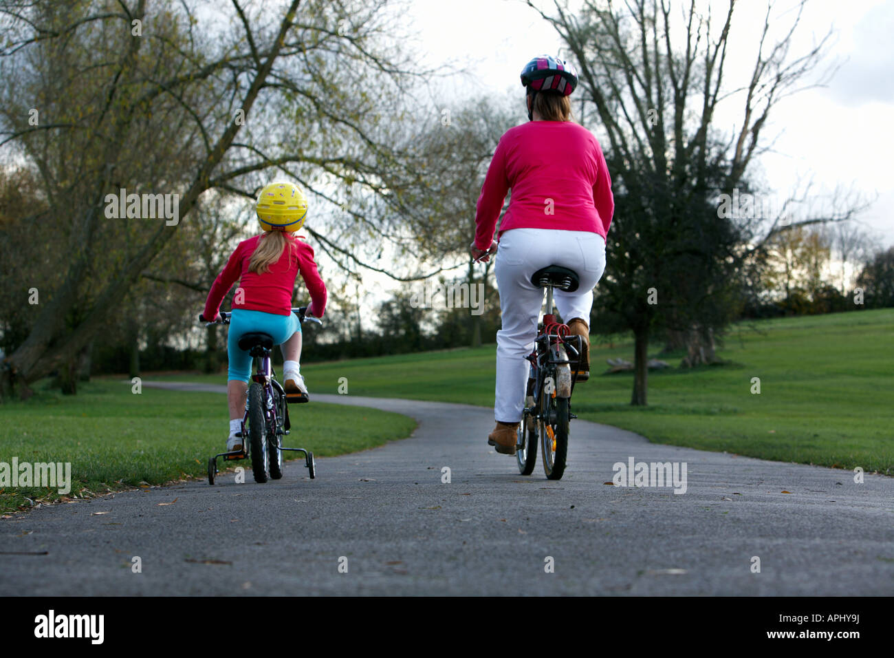 A young girl and a lady ride push bikes through a park Stock Photo