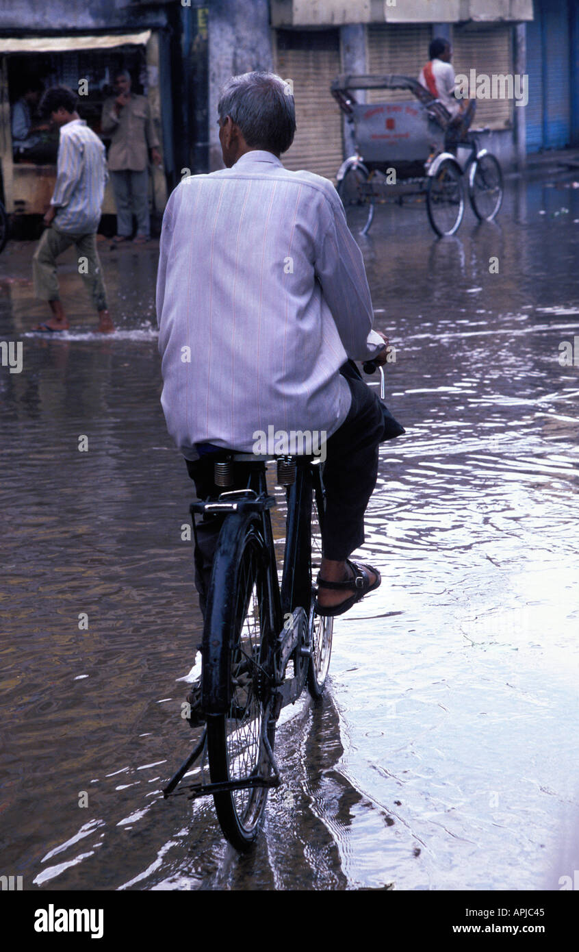 Man cycling along a water flooded street after downpour Varanasi India Stock Photo