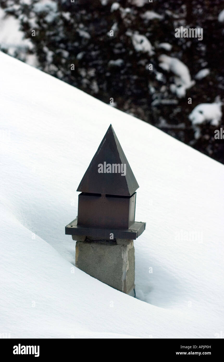 Chimney poking up through a snow covered chalet roof in the ski resort of Saas Fee in Wallis mountain range in Switzerland Stock Photo