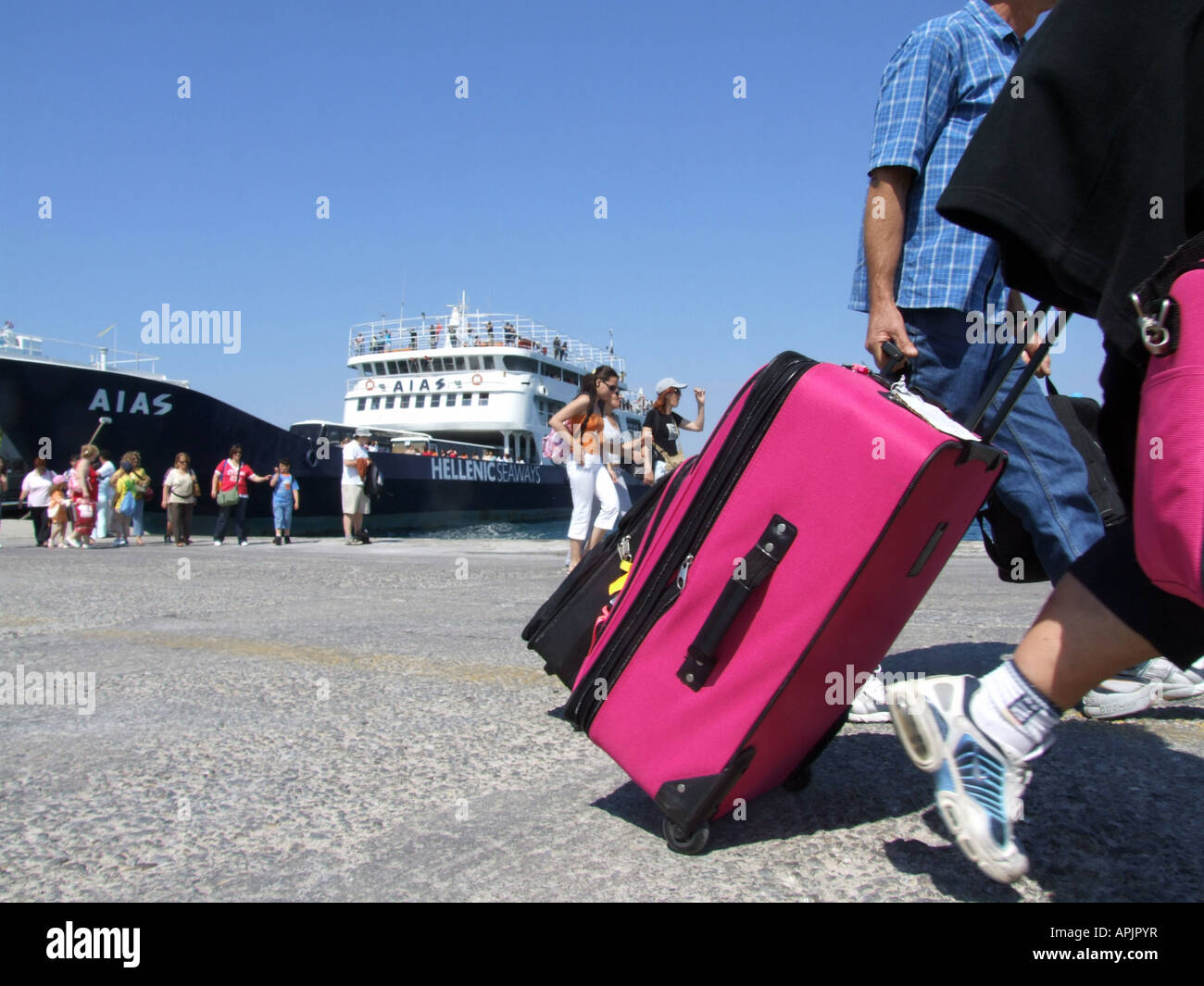 person pulling trolley luggage case in crowd in port, greece Stock Photo