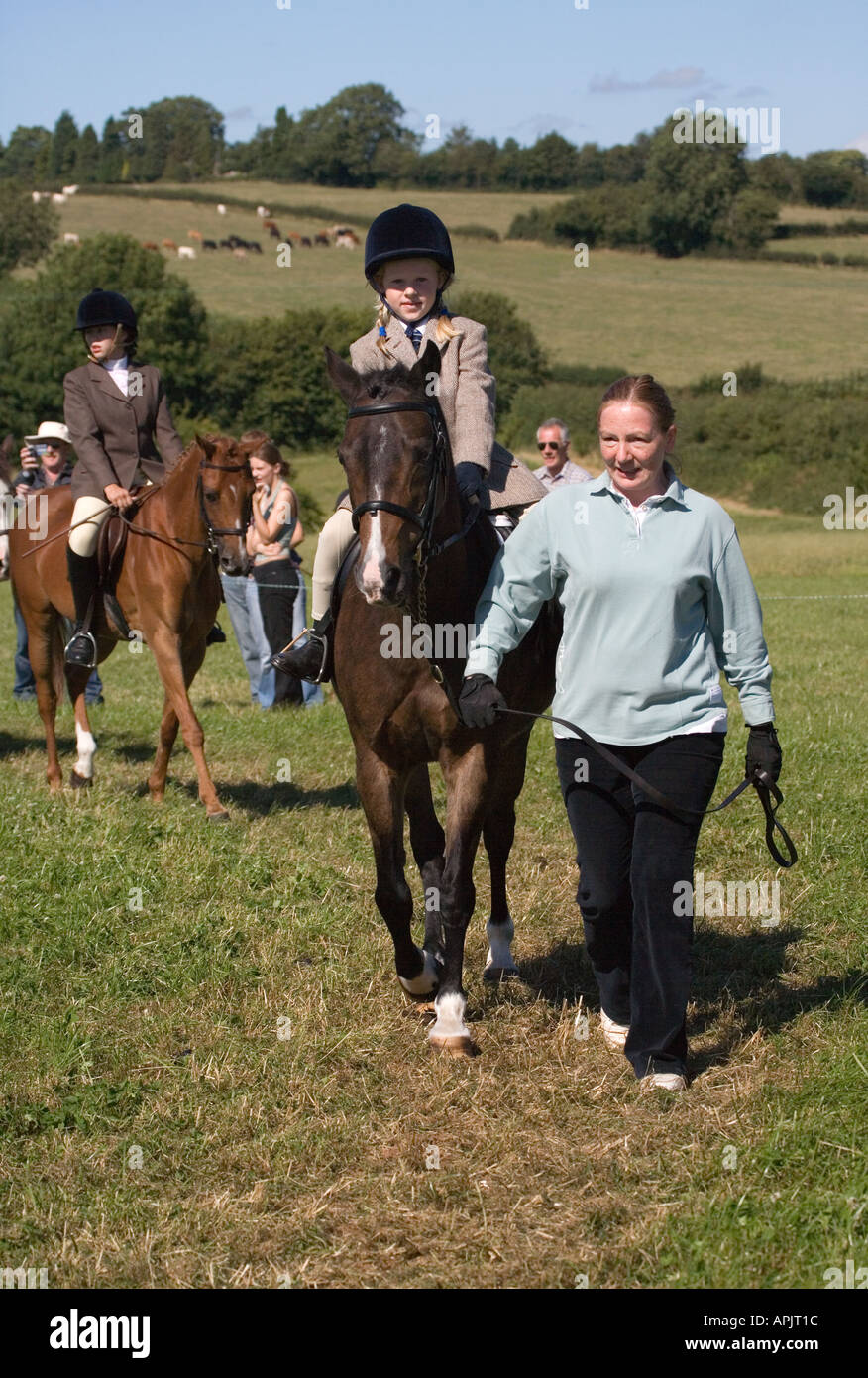 LITTLE GIRL AGED EIGHT RIDING PONY IN RIDING OUTFIT CLOTHES WITH ADULT LEADING PONY AT PONY CLUB EVENT UK Stock Photo