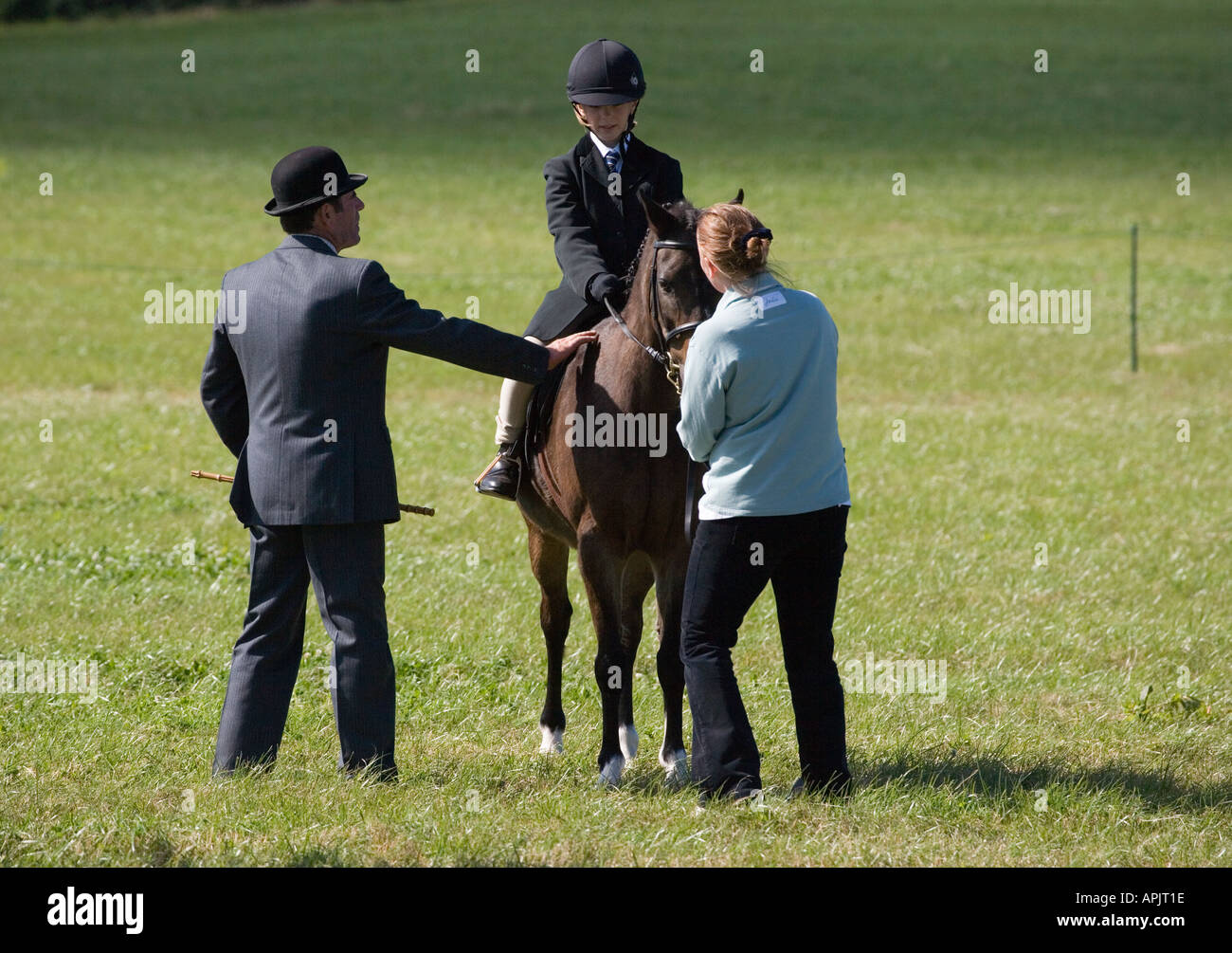 LITTLE GIRL ON PONY WITH BOWLER HATTED JUDGE AT RIDING EVENT UK Stock Photo