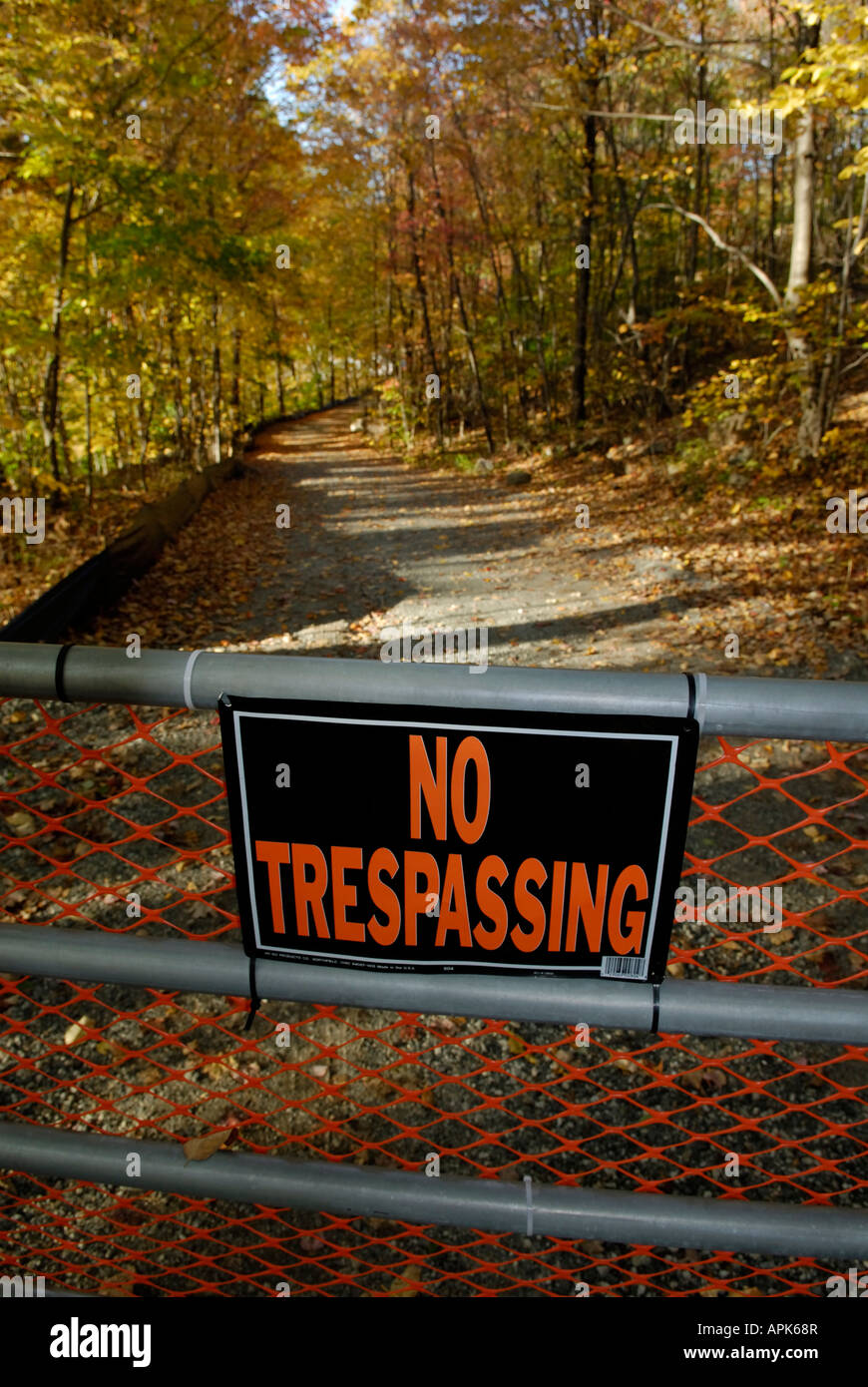 No trespassing sign and closed gate before a woods country road Stock Photo