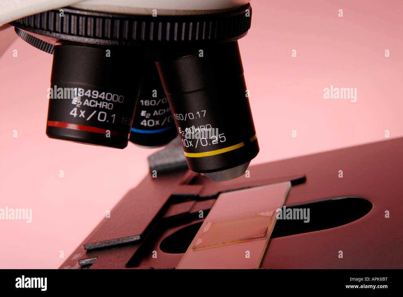 Close up of a microscope in a research lab showing the objective lenses and a slide Stock Photo