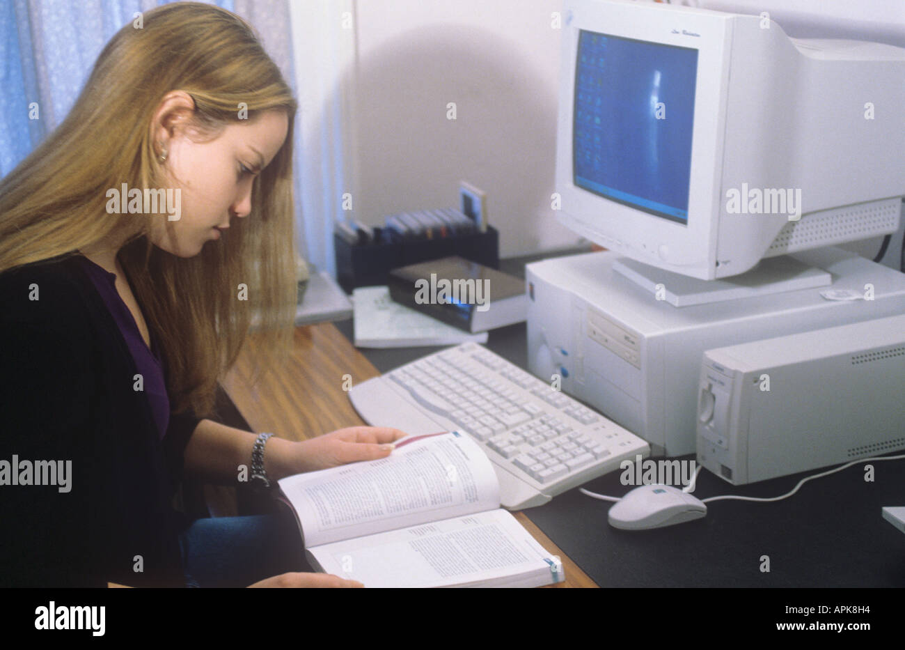 Teenage girl, sitting at desk with computer, reading Stock Photo