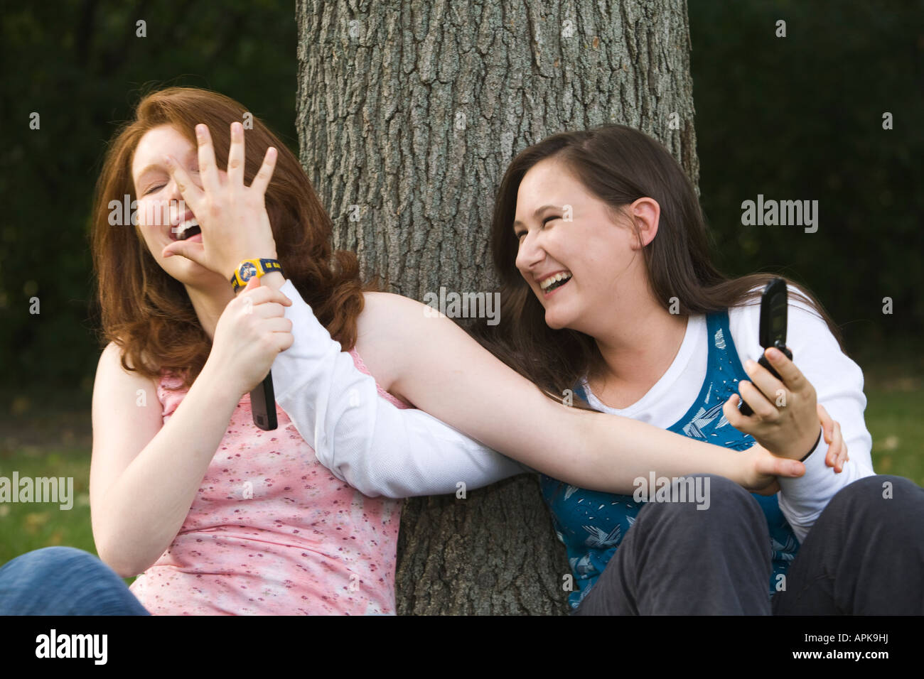 ILLINOIS Riverwoods Two teenage girls goofing around hand in front of face smiling and laughing sitting leaning tree trunk Stock Photo