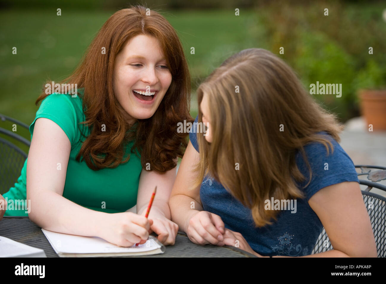ILLINOIS Riverwoods Two teenage girls goofing around together redhead erasing in notebook and laughing sitting at table Stock Photo