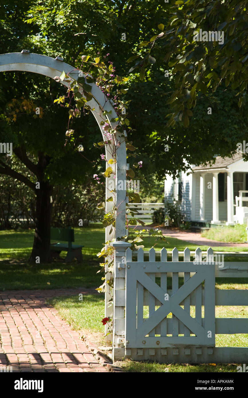 ILLINOIS Grand Detour White fence and arch with vine over brick sidewalk at John Deere Historic site white home in background Stock Photo