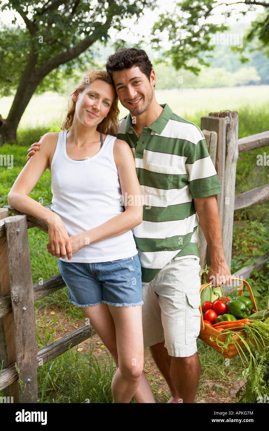 Husband and wife with vegetable basket standing by fence (portrait) Stock Photo