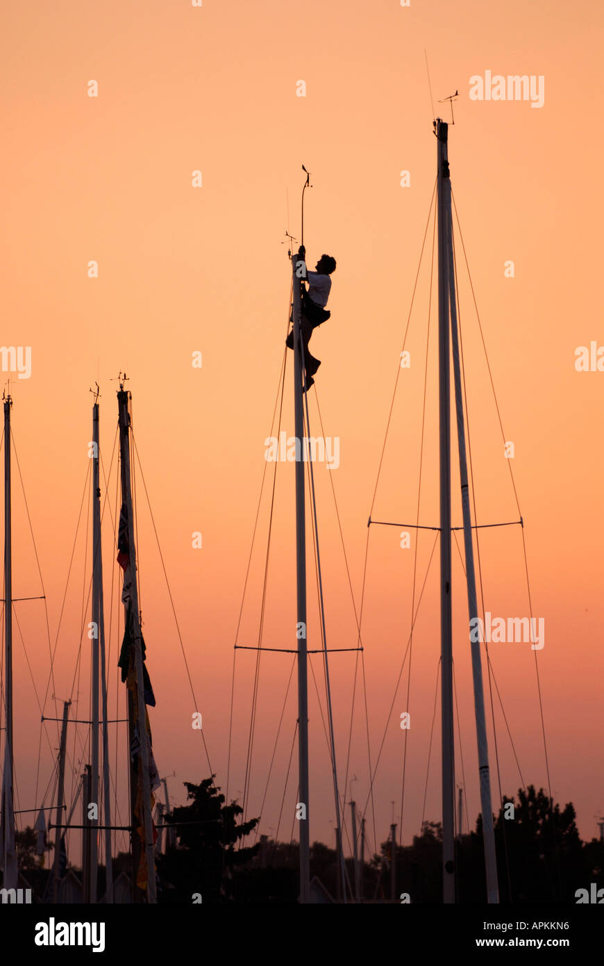 Male is silhouetted against the sky while climbing and working on a sailboat mast Stock Photo