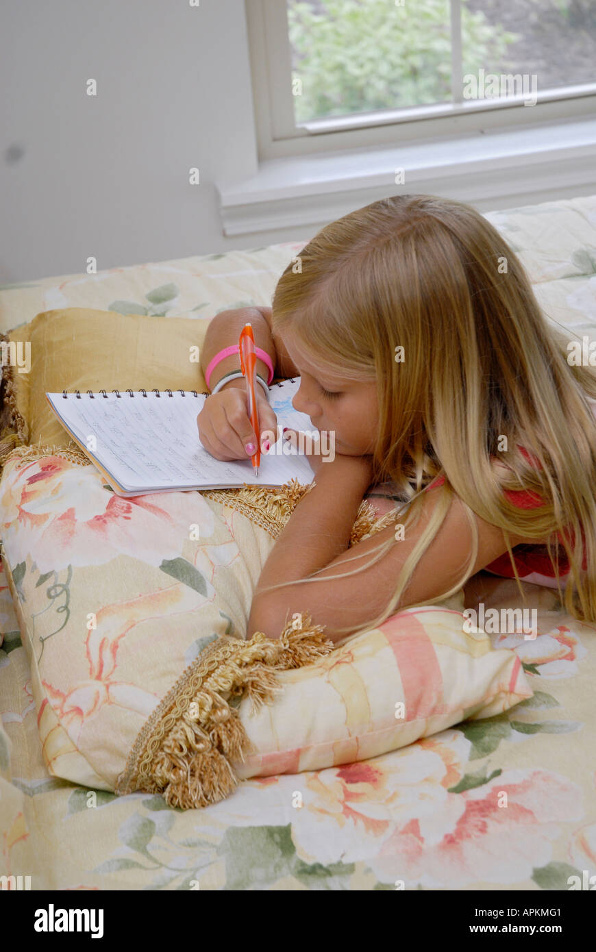 8 year old girl writes in her journal in her bedroom while laying 