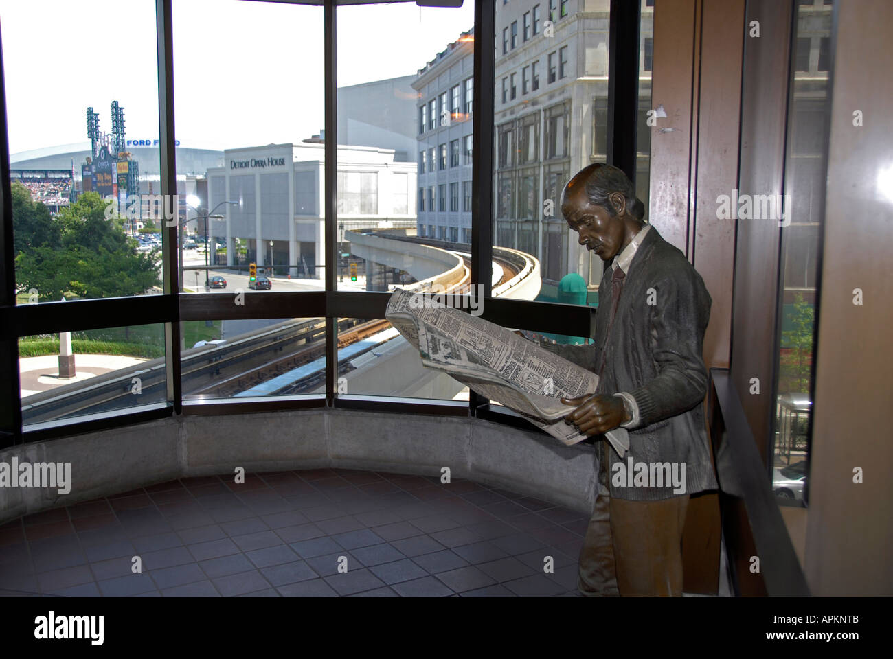 Statue of man reading newspaper while waiting for the People Mover rapid transit system in