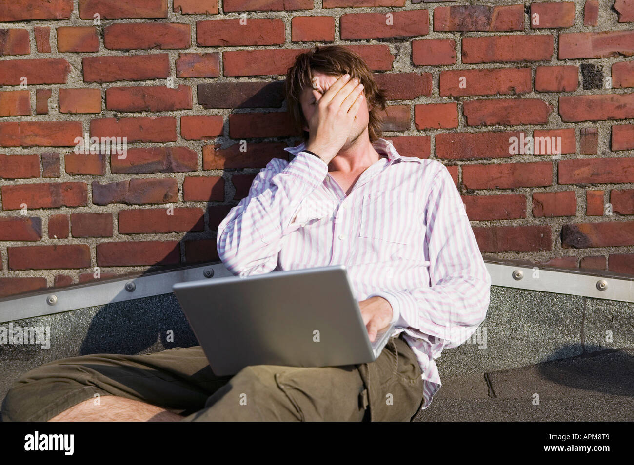 Man using laptop, leaning by wall Stock Photo
