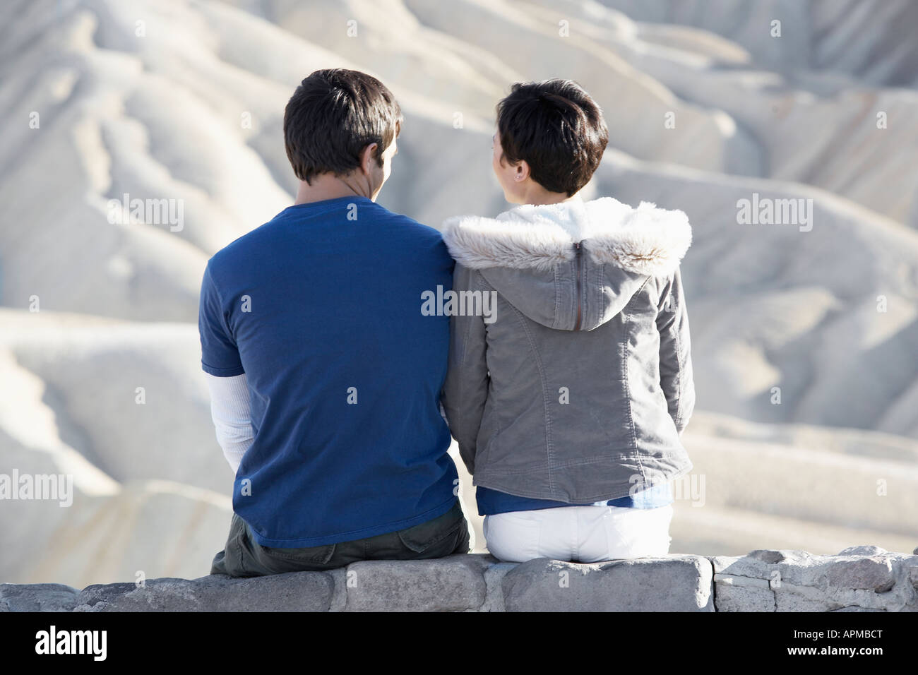 Couple sitting on stone wall in desert (rear view) Stock Photo