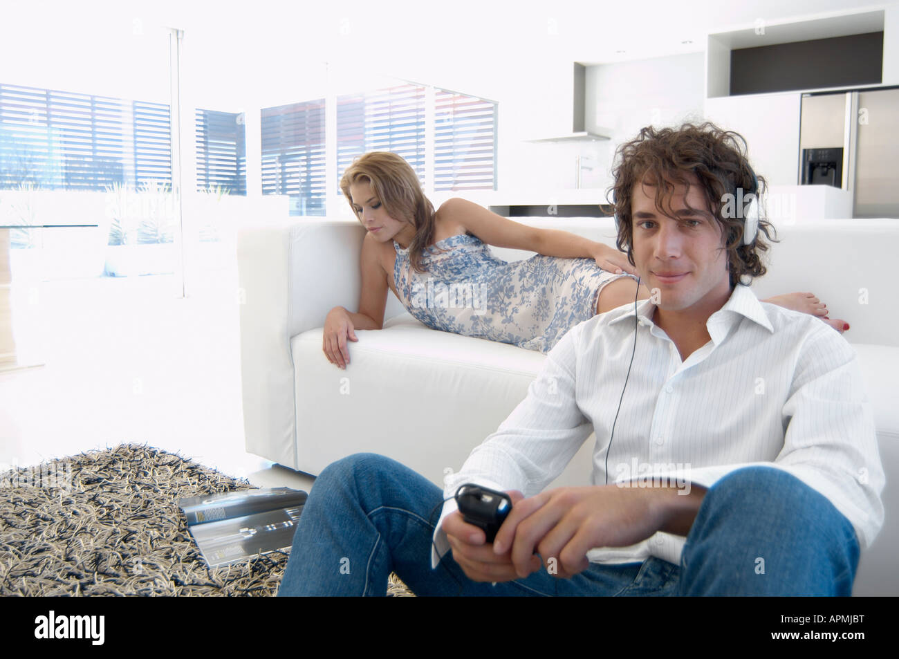 Young man listening to MP3 player, woman reading magazine on sofa Stock ...