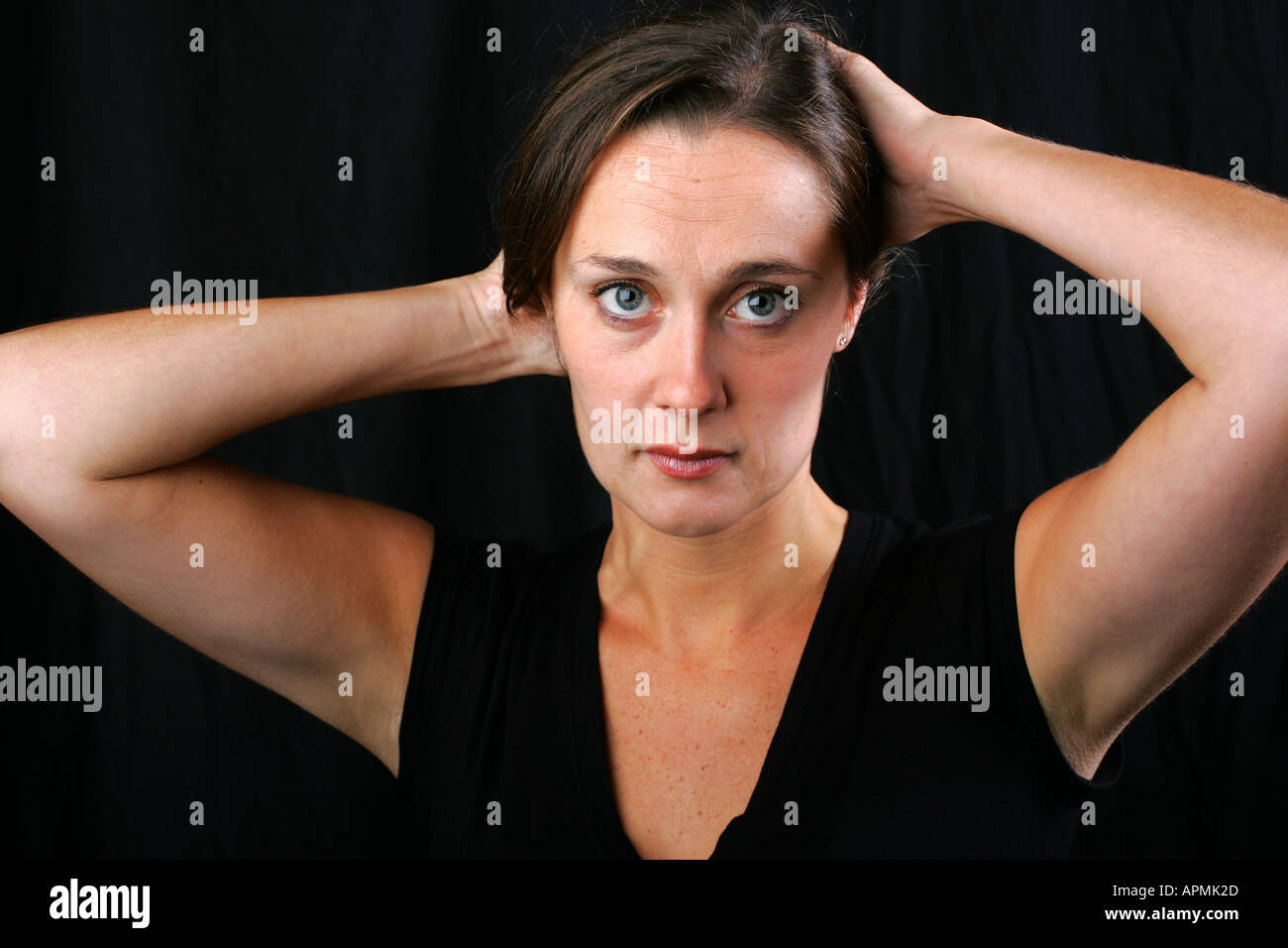 Pretty brunette woman holds her hands behind her head with emotionless cold unfeeling stoic dispassionate distant expression Stock Photo