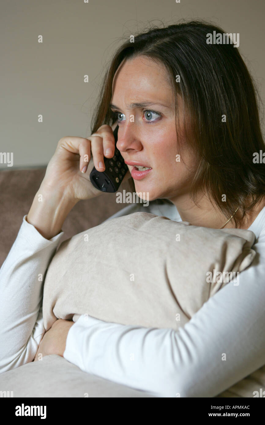Pretty young 20s 30s woman female looks anxious concerned during a cordless telephone conversation while relaxing at home Stock Photo