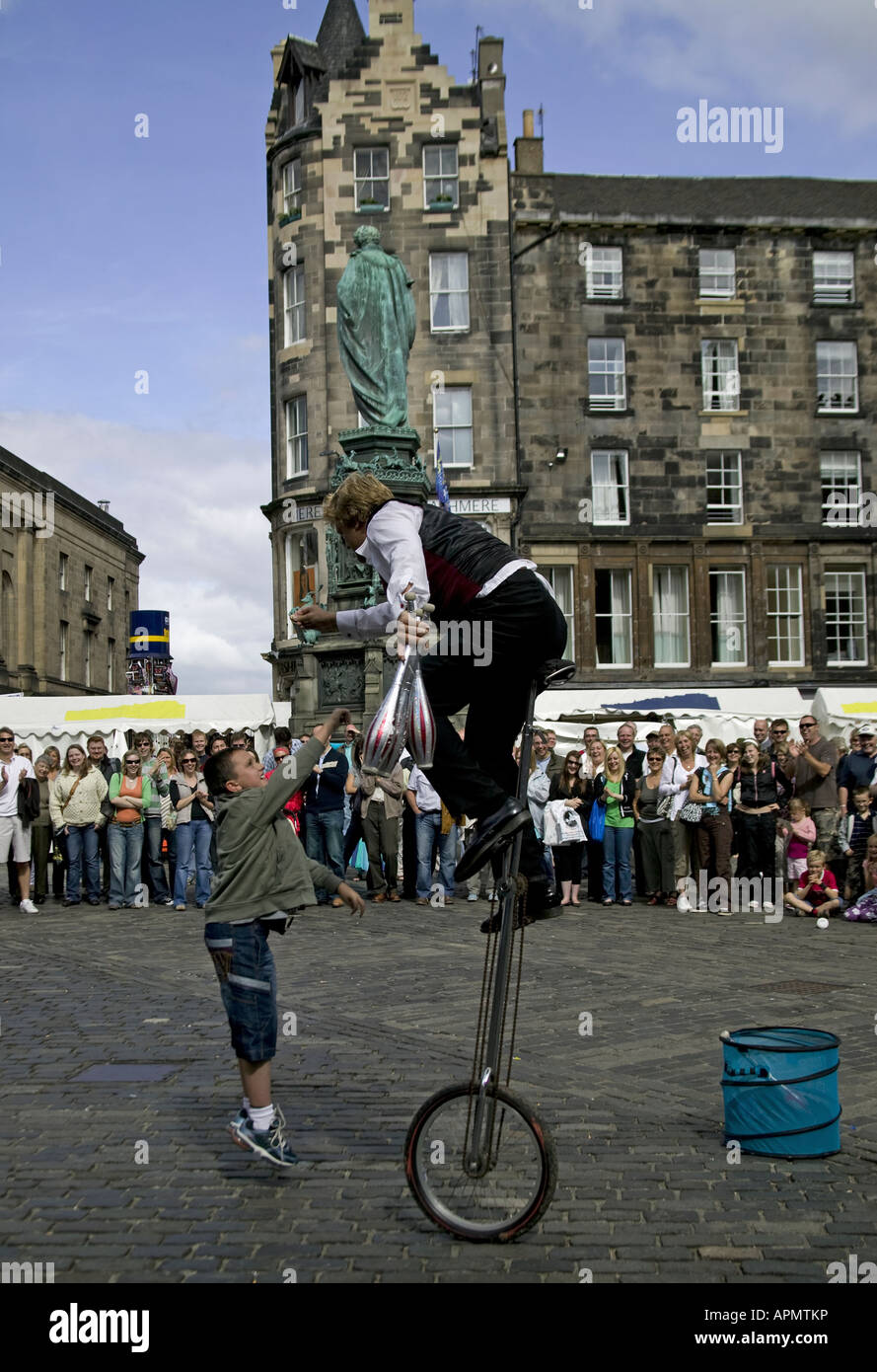 Edinburgh Fringe street performer on unicycle and young boy jumping for cash, Scotland UK Europe Stock Photo