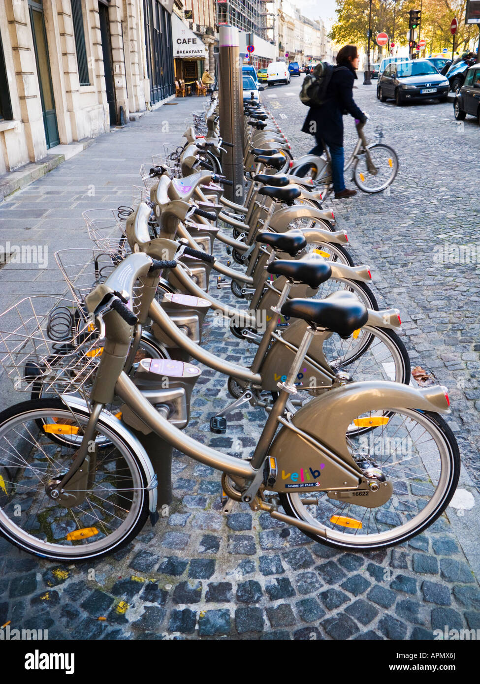 Cyclist rides away from a Velib cycle rack with bicycles for hire in Paris, France Stock Photo