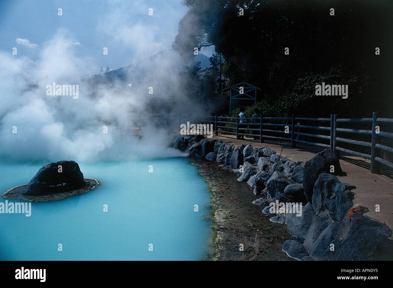 Clouds of steam rising from the milky blue waters of one of the eight hot springs known as Jigoku Hell Pools in which the waters reach boiling point at the hot spring holiday centre of Beppu with rocks forming a border around the pool Stock Photo