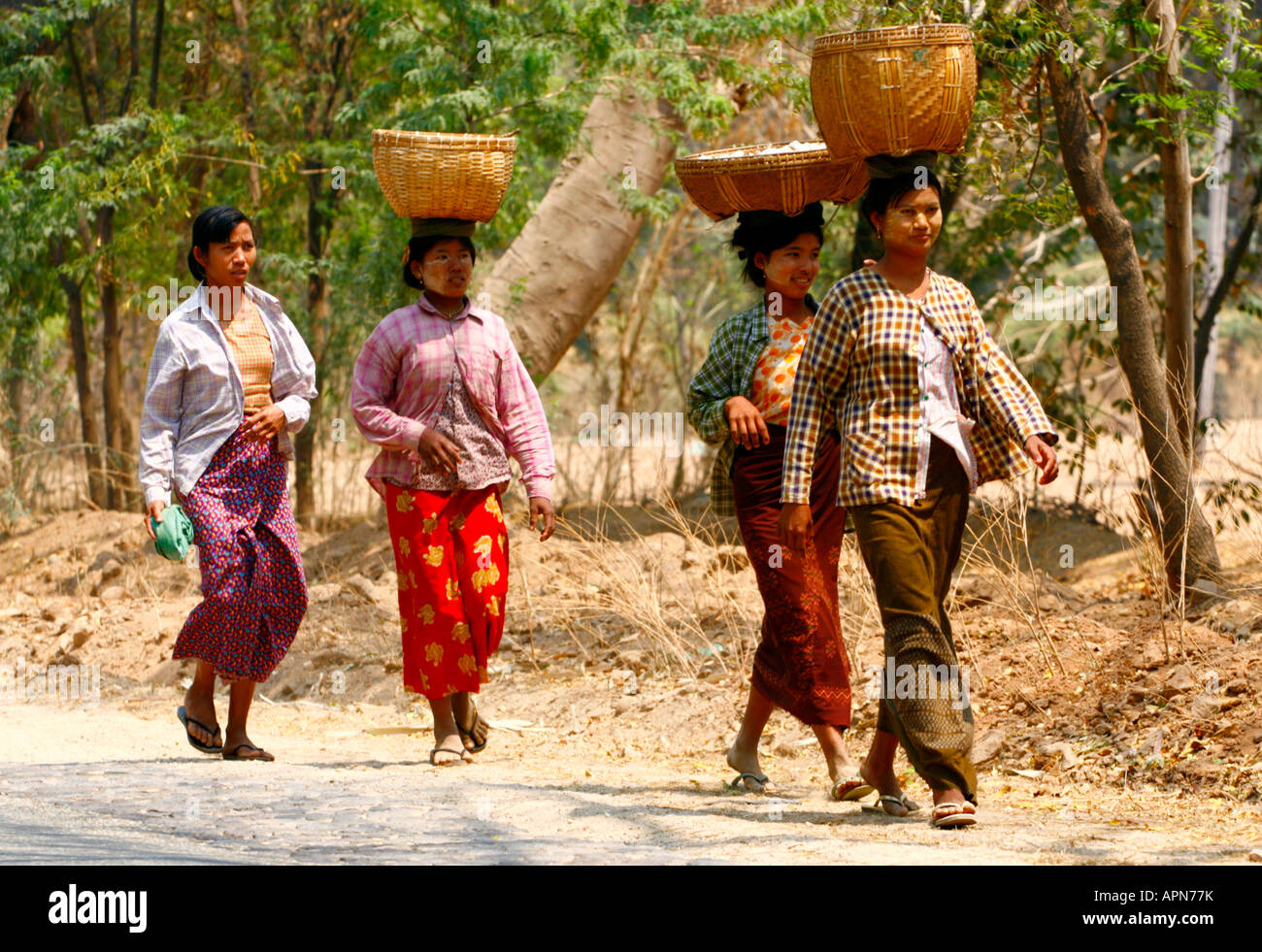 Four Burmese ladies walking down a dusty road, 3 carring baskets on their heads. Stock Photo