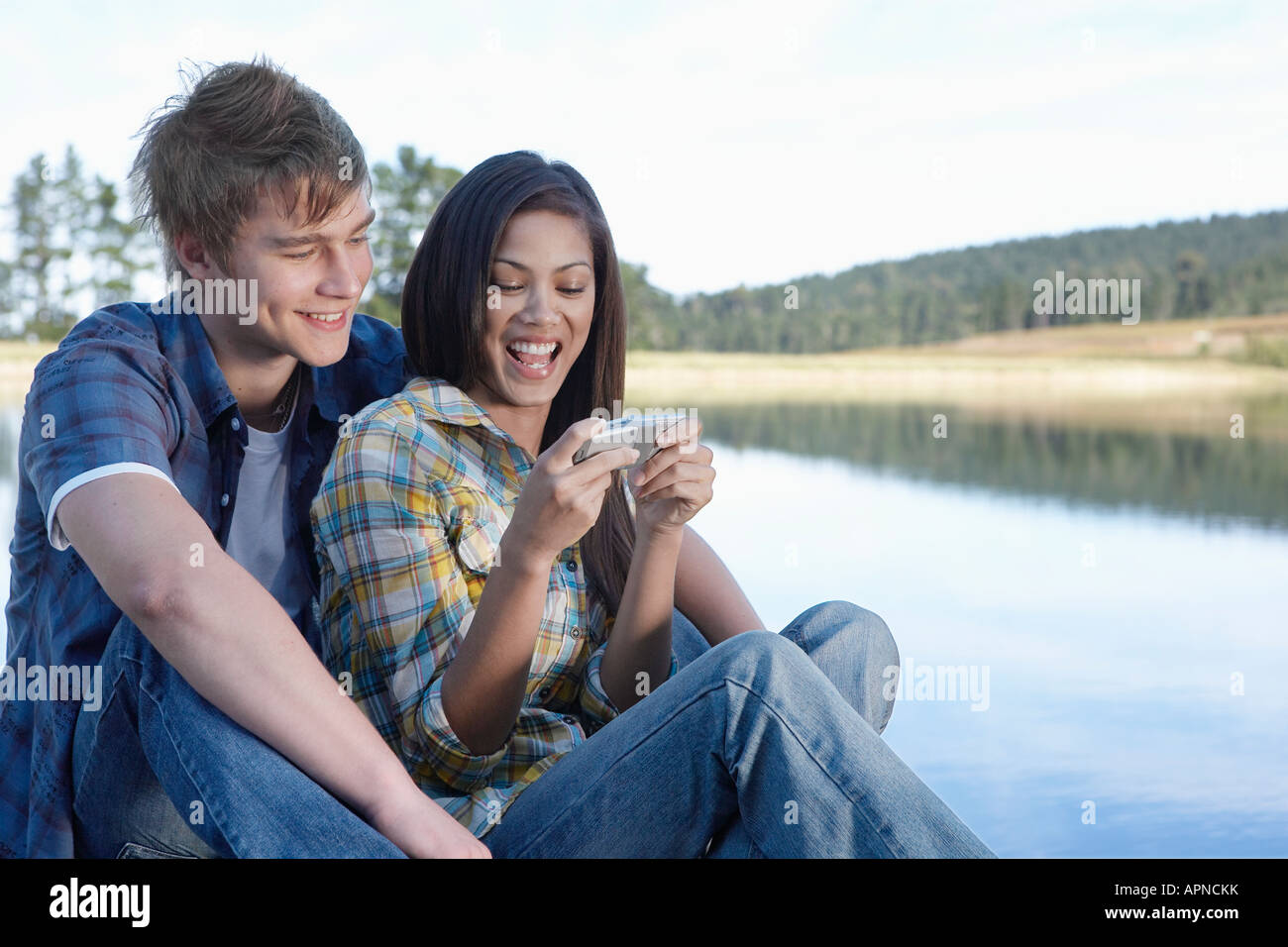 Teenage couple using mobile phone by lake Stock Photo