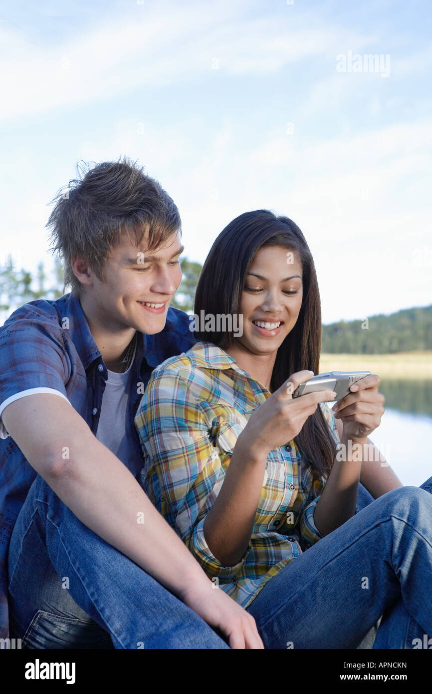 Teenage couple using mobile phone by lake Stock Photo