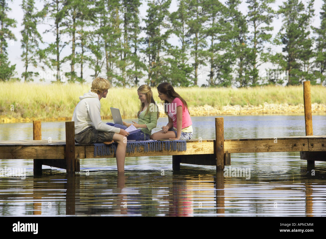 Three teenagers using laptop on jetty Stock Photo