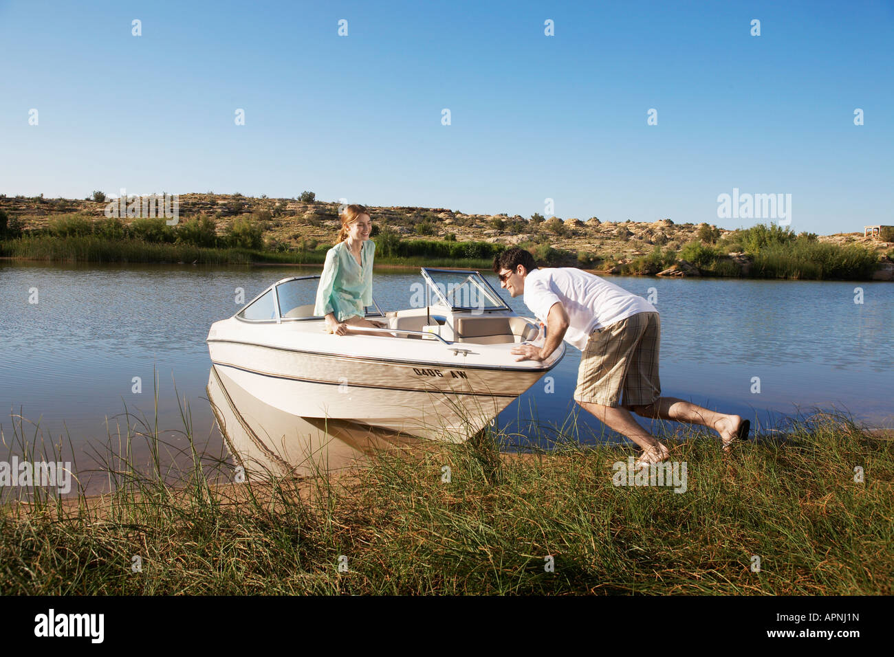 Young man pushing motorboat to lake, girlfriend looking Stock Photo - Alamy