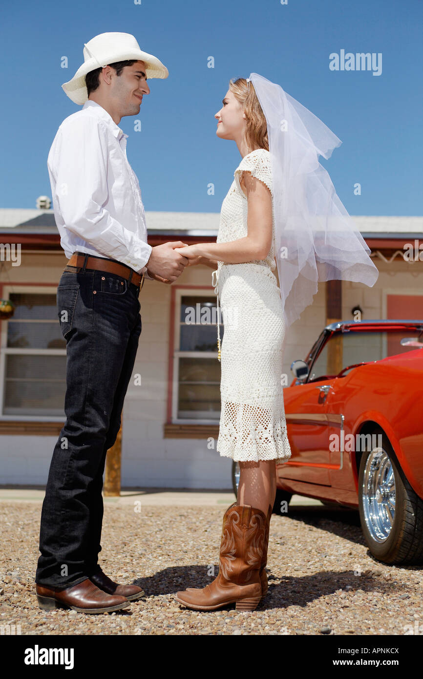 Newlyweds in cowboy attire holding hands and looking at each other Stock Photo