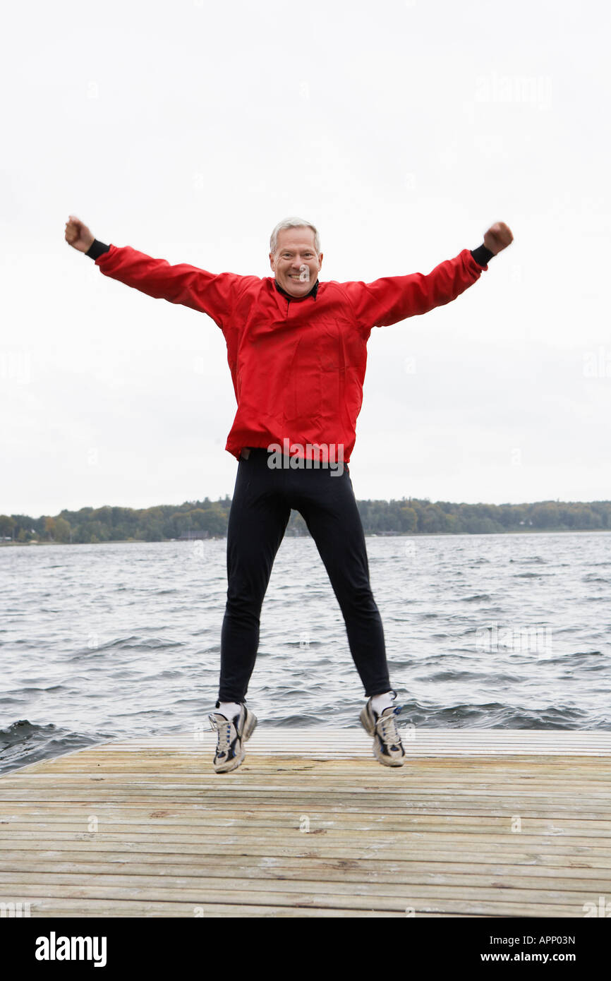 Senior man jumping on jetty Stock Photo