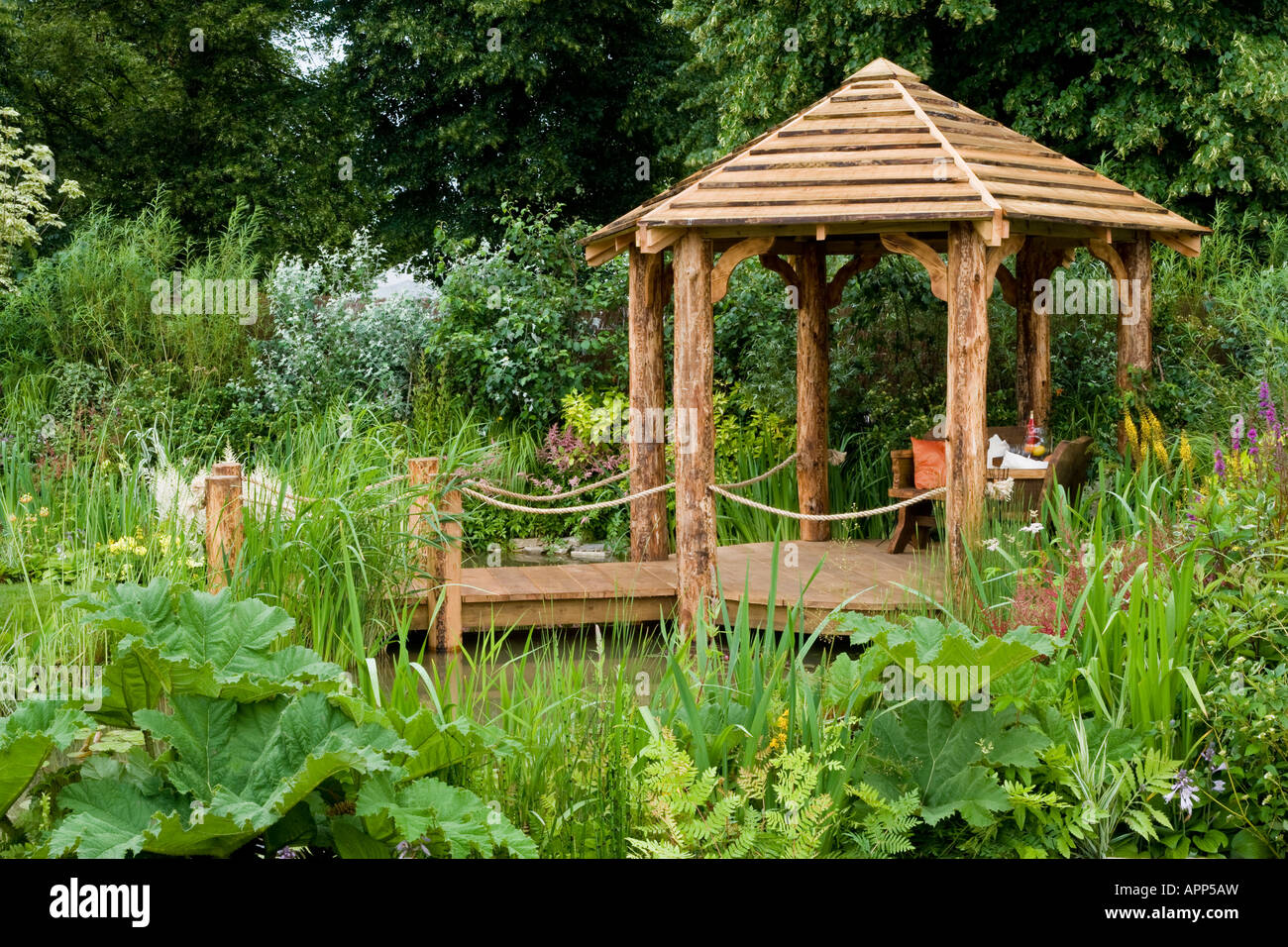 Rustic pergola on jetty over pool with chairs and table. Garden surrounds. Plants include Gunnera manicata and Equisetum hyemale Stock Photo