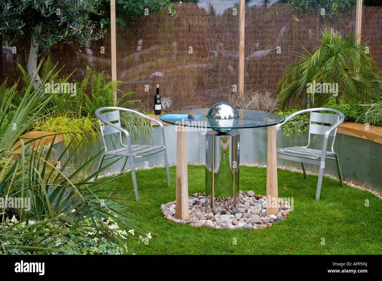 Small low maintenance garden with glass topped table and metal ball and metal chairs Stock Photo