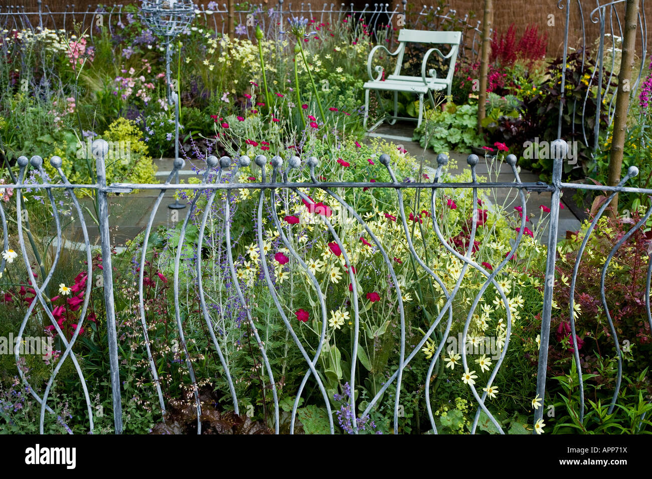 Decorative ironwork railings on edge of small garden with seat and ironwork bird station behind. Long depth of field Stock Photo