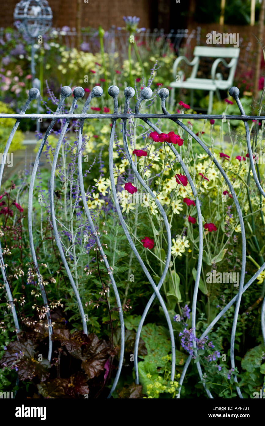 Decorative ironwork railings on edge of small garden with seat and ironwork bird station behind. Shallow depth of field Stock Photo