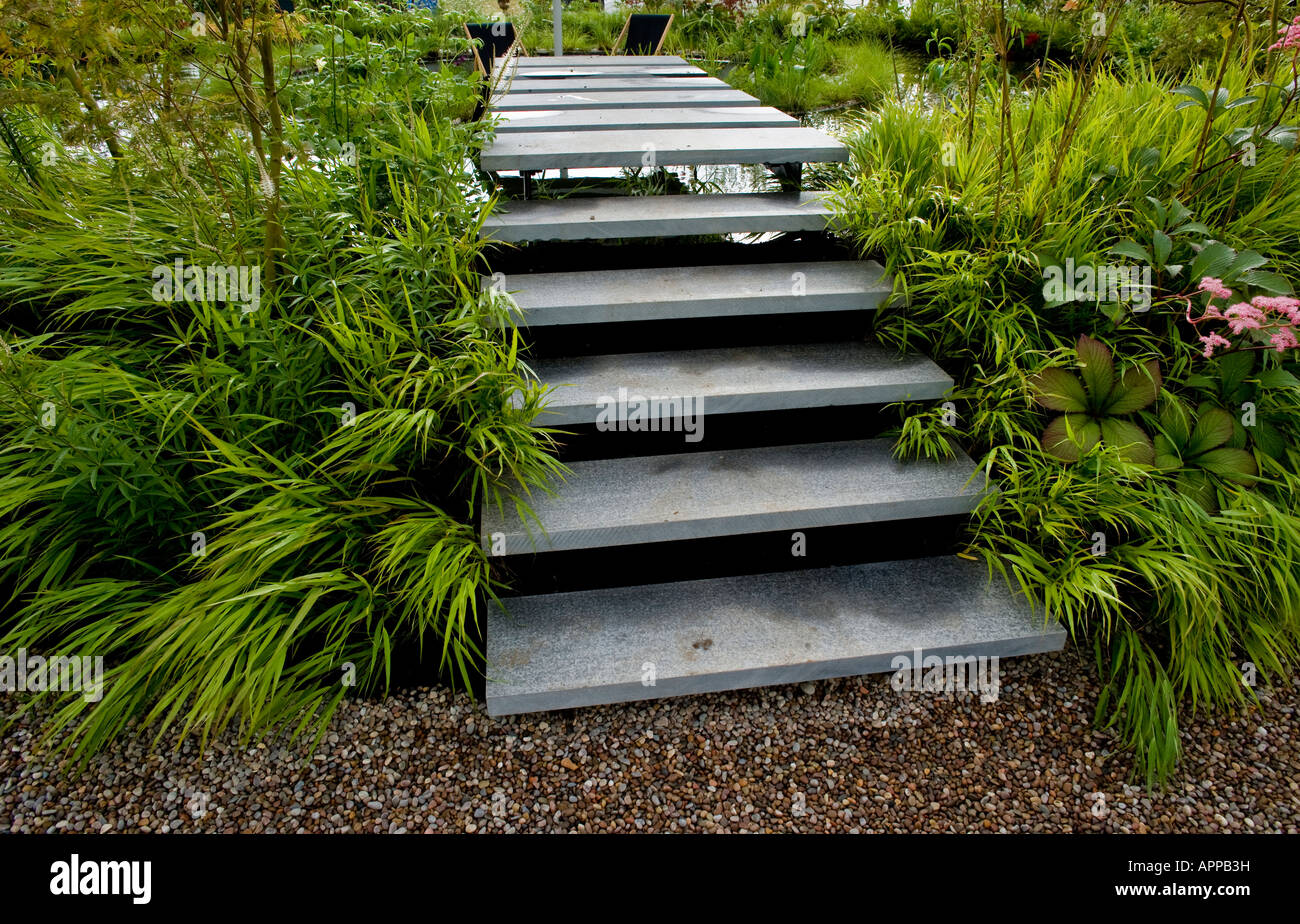 Steps up and over circular swimming pool Bamboo on either side with Veronicastrum virginicum rodgersia Stock Photo