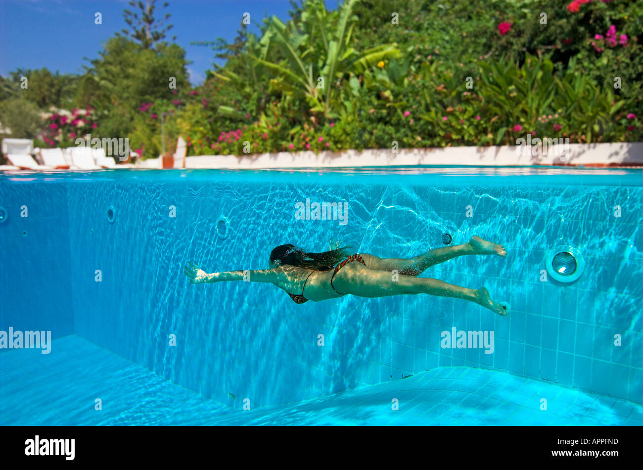 Woman in bikini diving underwater in swimming pool hotel above water