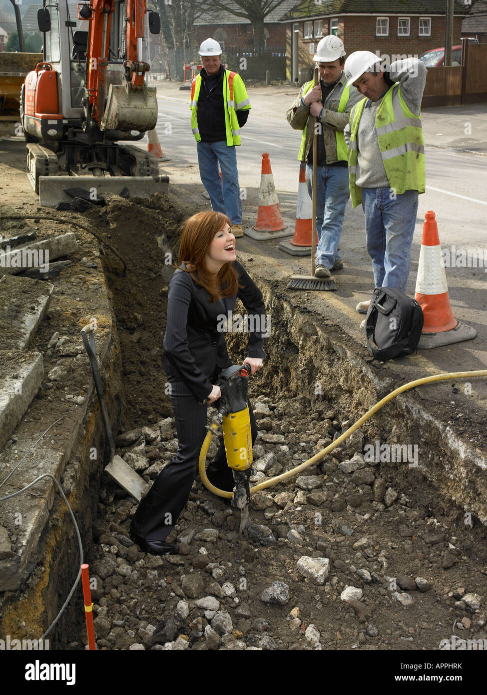 female office worker digging a trench with a jackhammer whilst workers