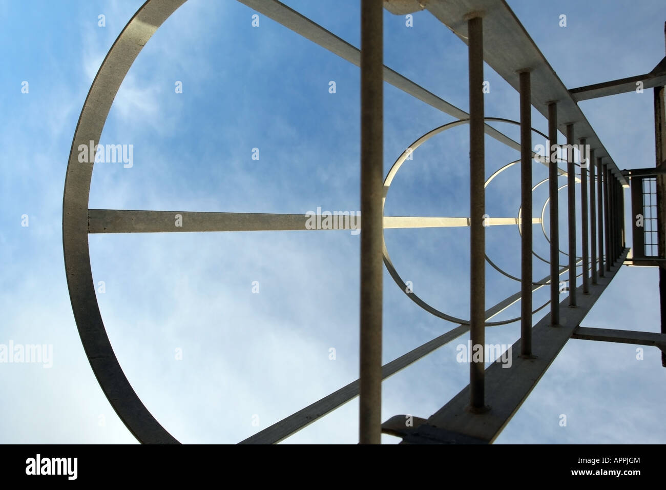 Looking up through a safety ladder with cage at blue sky Stock Photo