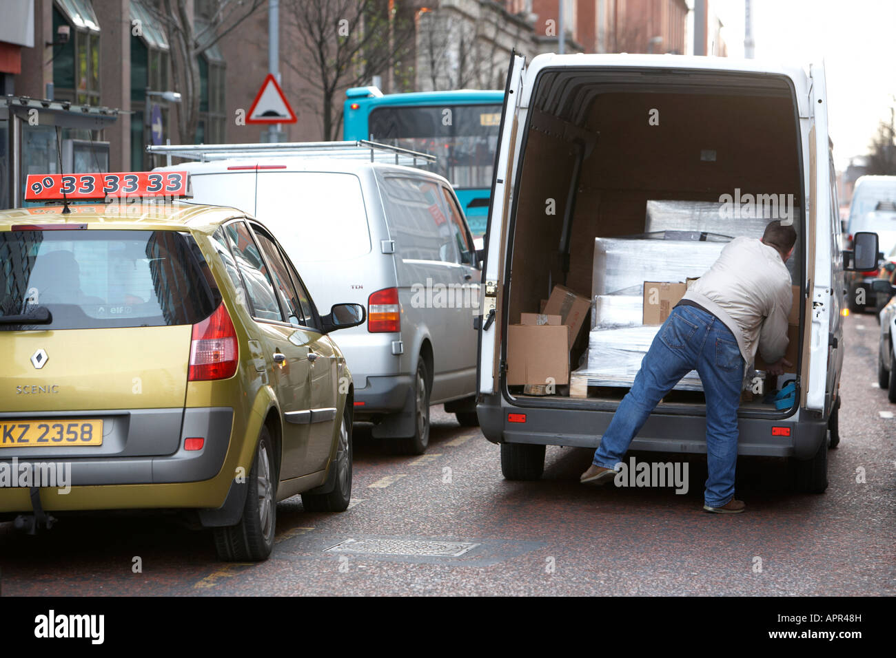 man unloading wrapped pallet boxes from van double parked in the road with traffic going past Belfast Northern Ireland UK Stock Photo