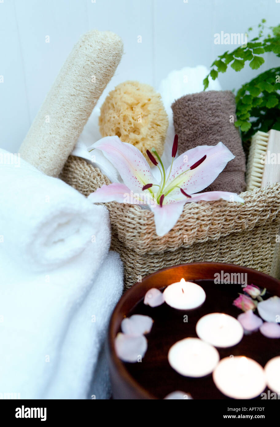 Spa setting with floating candles and rose petals, a basket filled with spa products including natural sponges folded towels and Stock Photo