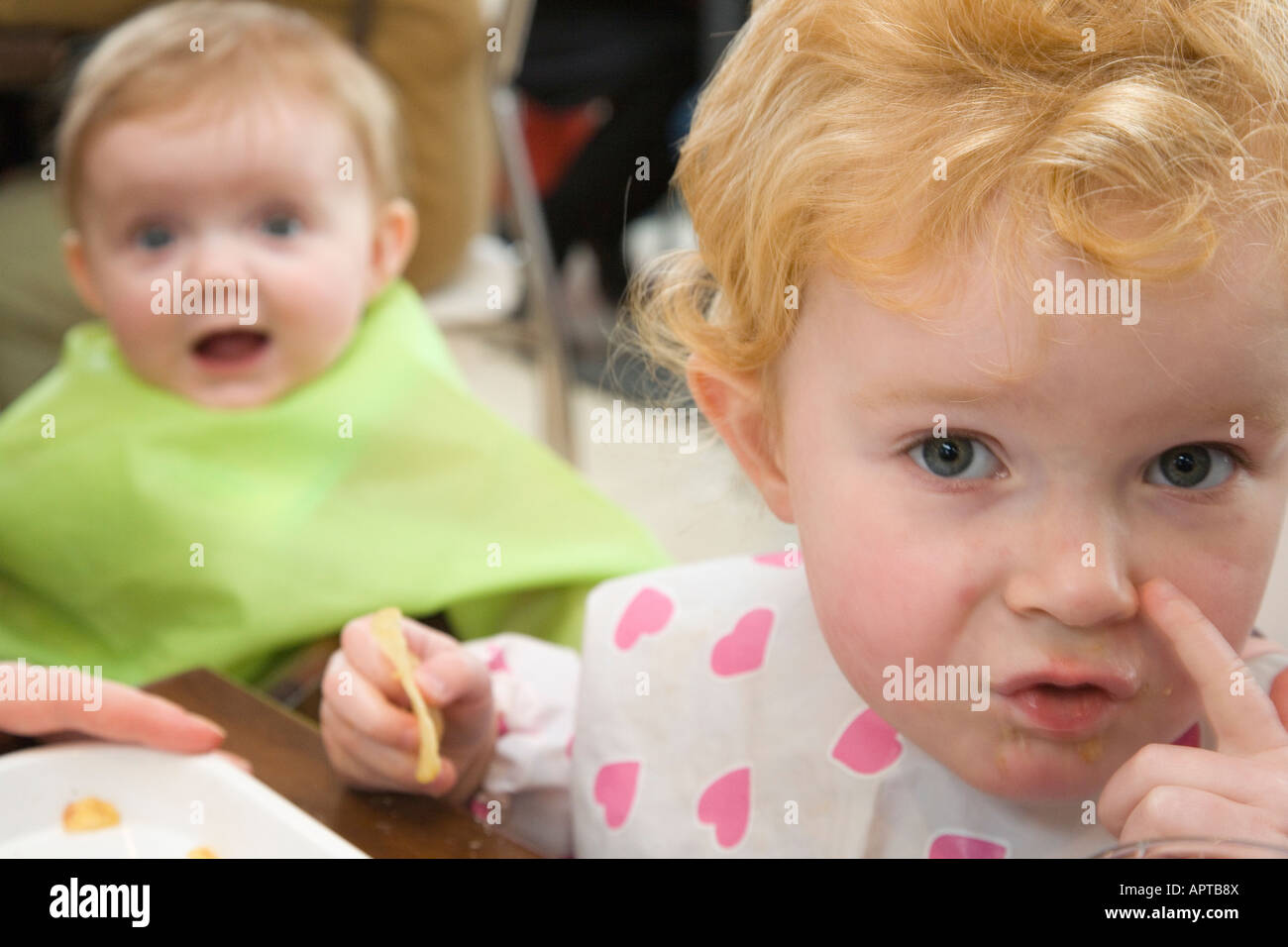 Toddler and baby sitting down for a meal wearing bibs Stock Photo